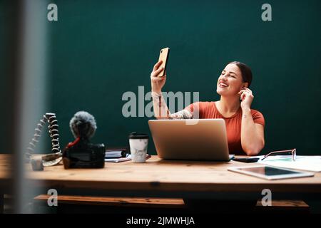 Another selfie. an attractive young businesswoman sitting alone against a green background and using her cellphone to take selfies. Stock Photo