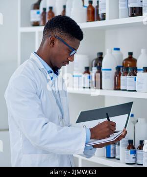 Theres a few things we need to stock up on. a focused young male scientist making notes while taking while doing stock on supplies inside of a Stock Photo