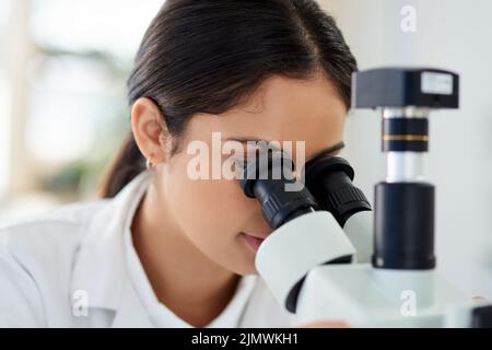 Things are a lot different under the lens. a young scientist using a microscope in a lab. Stock Photo