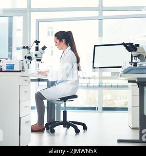 Looking at the new sample. a focused young female scientist conducting experiments inside of a laboratory during the day. Stock Photo