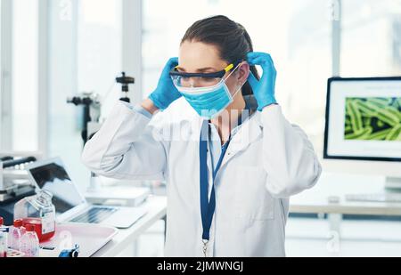 Safety first. an unrecognizable young female scientist putting on a protective face mask inside of a laboratory during the day. Stock Photo