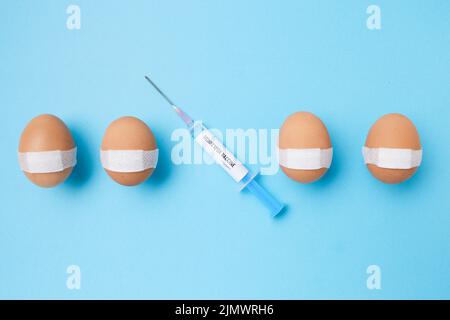flatlay with monkeypox vaccine syringe and vaccinated eggs with medical patch on blue background. Stock Photo