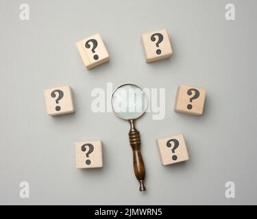 Wooden magnifier and cubes with question marks on gray background Stock Photo