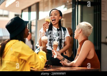We never say no to getting ice cream. three friends enjoying ice cream cones while out in the city. Stock Photo
