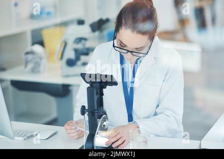 Getting closer and closer to my goal. a focused young female scientist looking through a microscope while doing tests inside of a laboratory. Stock Photo