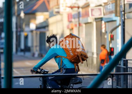 A Just Eat bike delivery rider with a large orange backpack with Just Eat logo cycles along a street in Southend on Sea, Essex Stock Photo