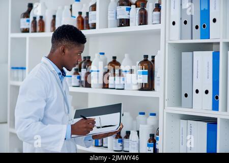 Everything seems to be in place. a focused young male scientist making notes while taking while doing stock on supplies inside of a laboratory during Stock Photo