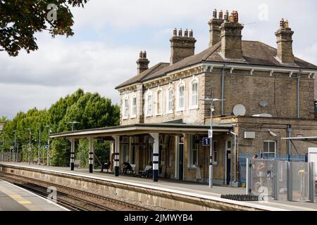 Chertsey Railway Station building, platform and track with people waiting for a train. Stock Photo