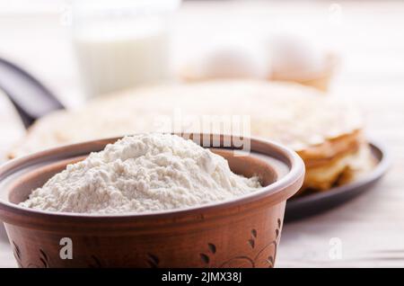 Stack of French crepes in frying pan on wooden kitchen table with milk eggs and flour aside Stock Photo