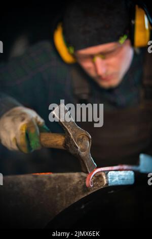A man working blacksmith making a detail out of hot metal Stock Photo
