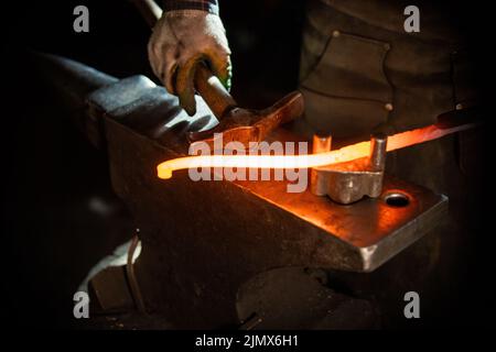A man blacksmith making a detail out of hot metal using a hammer and anvil Stock Photo