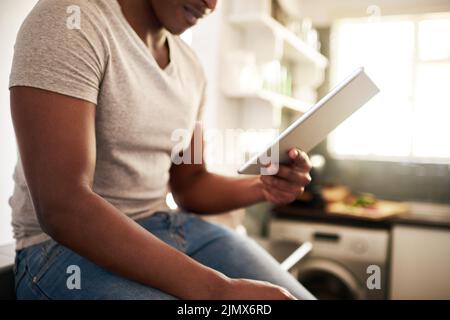 Lets see whats trending today. an unrecognizable man using a digital tablet while sitting on the kitchen counter at home. Stock Photo