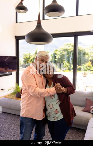 Portrait of cheerful multiracial senior friends embracing and dancing against window in nursing home Stock Photo