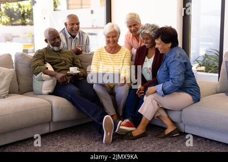 Biracial senior woman using laptop with multiracial friends while sitting on sofa in nursing home Stock Photo
