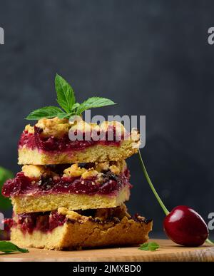 Square slices of cherry crumble lie in a stack on a black background Stock Photo
