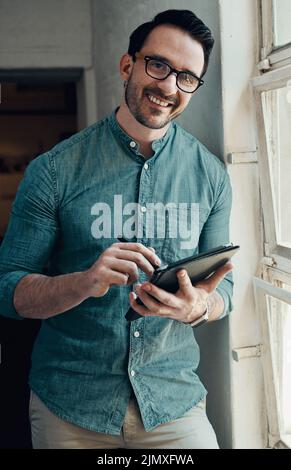I can do most of my work using this smart device. Cropped portrait of a handsome young businessman smiling while using a digital tablet in a modern Stock Photo