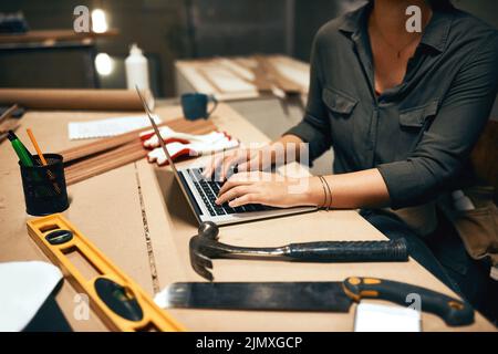 There is no substitute for hard work. an unrecognizable young female carpenter working on her laptop in the workshop. Stock Photo