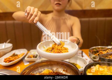 Lady tonging Korean noodle in Korea restaurant, enjoying traditional asian food. Food and travel concept. Selective focus. Stock Photo