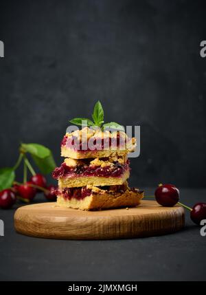 Square slices of cherry crumble lie in a stack on a black background Stock Photo