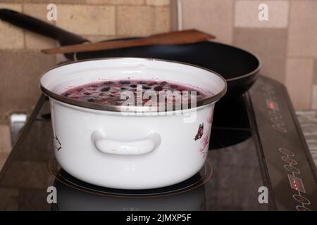 homemade fruit compote with cherry boils on the stove in the kitchen in a white saucepan, fruit compote in a saucepan Stock Photo