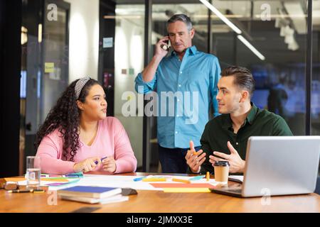 Manager talking on smart phone looking at multiracial colleagues discussing strategy in office Stock Photo