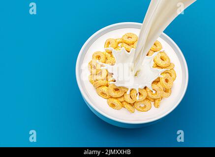 Corn rings with pouring milk on blue background, top view Stock Photo
