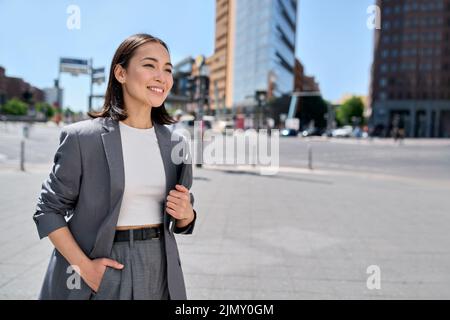Young confident happy Asian business woman entrepreneur standing on city street. Stock Photo