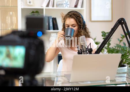 Woman vlogger with headphones looking at laptop and recording video on professional camera Stock Photo
