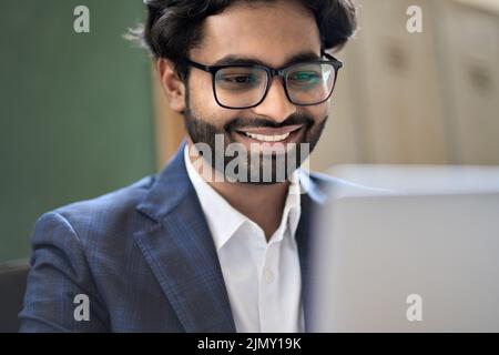 Happy indian young business man executive wearing suit working on laptop. Stock Photo