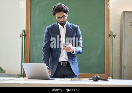 Young indian business man using phone working on laptop in office. Stock Photo