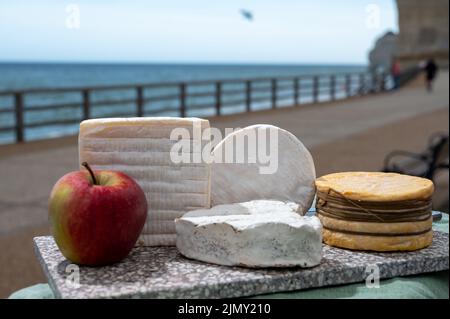 Four famous cheeses of Normandy, squared pont l'eveque, round camembert cow cheese, yellow livarot, heartshaped neufchatel and view on promenade and a Stock Photo