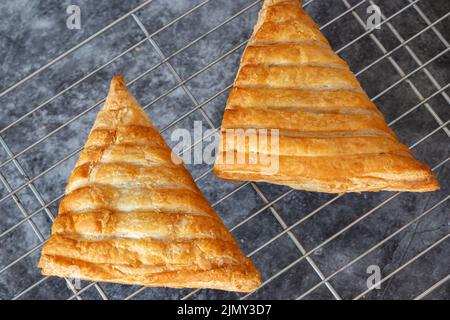 Apple turnover, freshly cooked, cooling down on a metal cooling rack. On a dark stone background Stock Photo