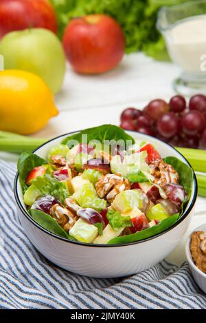 Waldorf salad of apples, celery stalks, walnuts, grapes, lettuce in a white salad bowl with ingredients on an old rustic white wooden table. Selected Stock Photo