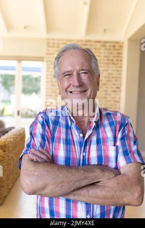 Portrait of cheerful caucasian senior man with arms crossed wearing checked pattern shirt at home Stock Photo