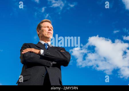 Low angle view businessman standing with folded arms against sky Stock Photo
