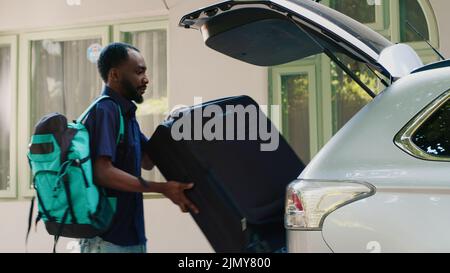 Joyful couple loading vehicle trunk with baggage and trolleys while getting ready for holiday citybreak departure. People putting voyage luggage and trolleys inside car while going on field trip. Stock Photo