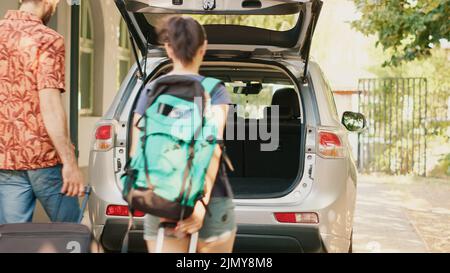 Casual couple putting voyage baggage inside vehicle trunk while getting ready for summer holiday citybreak. Married people loading baggage and trolleys inside car while going on field trip vacation. Stock Photo