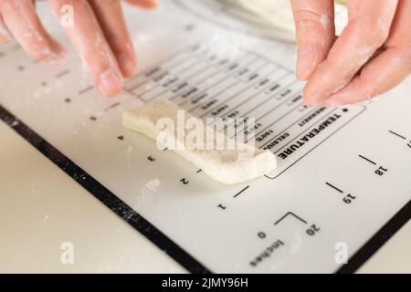 Cook's hands measuring the length in inches of a cut piece of dough on a kitchen mat with markings, selective focus and close-up Stock Photo