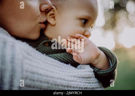 Mother holding her little baby son wearing knitted sweater during walk in nature, close-up Stock Photo