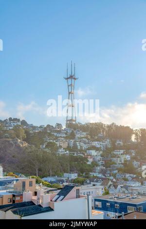 Faint view of Sutro Tower against the sunset sky in San Francisco, California. There is a view of dense houses and trees on the slope of the mountain Stock Photo