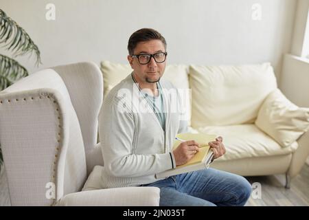 Friendly psychologist with clipboard, leaning at wall in office, empty space Stock Photo