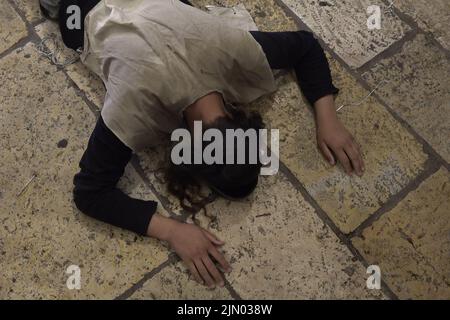 A religious Jew wearing jute bag to signify grief prostrates on the ground in prayer as Jews mourn at Bab al-Qattanin Gate, which leads to the Temple Mount in the Muslim Quarter, on the Jewish feast of Tisha B'Av on August 7, 2022 in Jerusalem, Israel. Jewish people around the world read from the Book of Lamentations, marking the beginning of Tisha B'Av, the annual fasting day commemorating the destruction of the First and Second Temples in Jerusalem Stock Photo