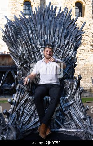 EDITORIAL USE ONLY Reality TV star Sam Thompson sits on the Iron Throne outside the Tower of London to mark the launch of the Game of Thrones prequel, House of the Dragon, airing on Sky and streaming service NOW from August 22. PA PHOTO Picture date: Monday August 8, 2022. The throne is being displayed at the Tower of London today and tomorrow, ahead of the House of the Dragon premiere next week in Leicester Square. Fans and Visitors to the Tower of London will be able to discover more about the news series via a QR code next to the Iron Throne. The Throne will then be touring the country, inc Stock Photo