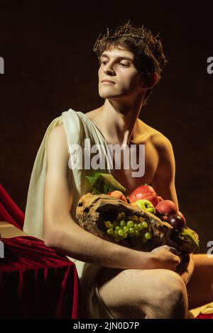 Creative remake of painting boy with a basket of fruit. Young handsome man over dark vintage background. Italian baroque style, art, creativity Stock Photo