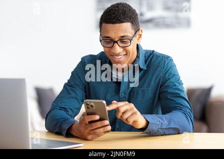 African American man entrepreneur in modern office looking at screen typing message with mobile phone Stock Photo