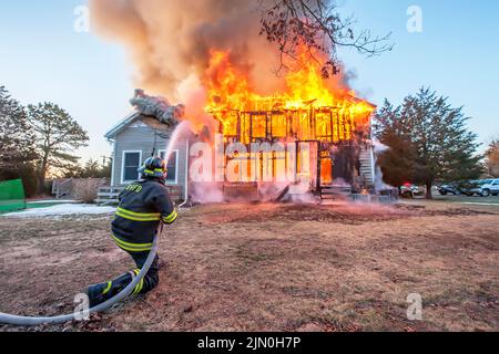 A firefighter sprays water onto the fully-involved building as shortly before 6:00 a.m. on Saturday, March 8th, 2014 the Bridgehampton Fire Department Stock Photo