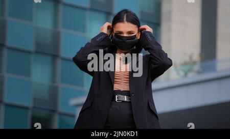 Young hispanic girl standing on city building background looking at camera businesswoman wearing medical protective mask protects health from viral Stock Photo