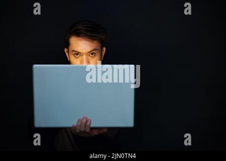 Serious hacker looking at camera over laptop screen when working in dark room Stock Photo