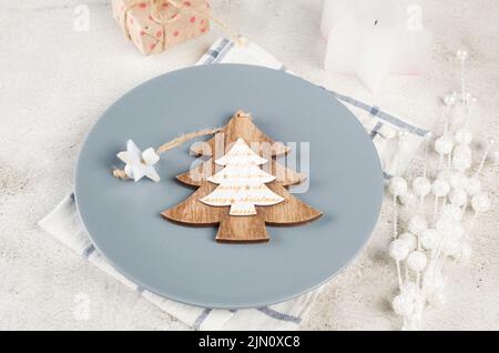 Christmas table setting. Top view of empty grey plate with black cutlery and craft wooden decorations on light table. Event table decoration. Stock Photo
