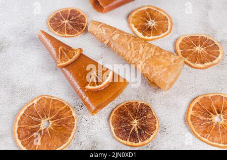Assorted pastille rolls. Fruit leather pastille cones and dried oranges on light grey bacground. Healthy eating concept, snack, no sugar. Stock Photo